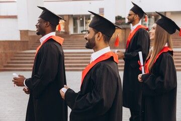 Group of Diverse Graduates in Caps and Gowns Celebrating Graduation Day Outdoors