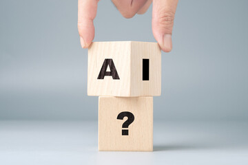 A hand places a wooden cube with the letters AI on another wooden cube with a question mark, using...