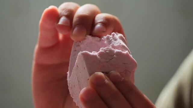 A close-up shot of a hand holding a pink marshmallow zefir