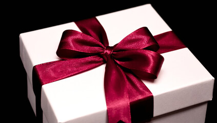 An elegant white gift box with a burgundy ribbon and bow, isolated on a black background, symbolizing a holiday or a surprise.