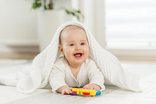 Laughing baby under blanket with toy. Baby care concept.