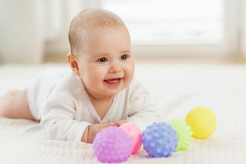 Baby care concept. Baby enjoys playtime with colorful sensory balls on a soft blanket indoors