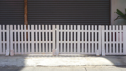 White prefabricated wooden fence on patio in front of the old garage with sunlight and shadow on...