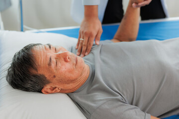 An elderly patient undergoes leg physiotherapy on a treatment bed while being carefully assisted and advised by a healthcare specialist.