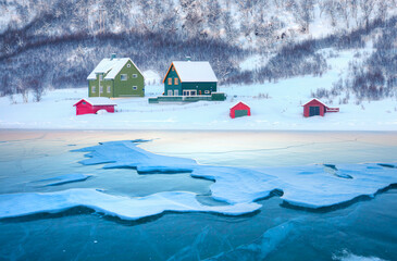 Wooden houses on the banks of the Norwegian fjord, beautiful mountain landscape in winter
