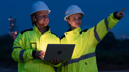 caucasian white engineers in safety uniforms and helmets using laptop and radio for site communication. Concept of teamwork, inspection, and operations at an industrial facility.Construction of Oil, 