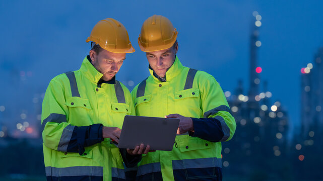 caucasian white engineers in safety uniforms and helmets using laptop and radio for site communication. Concept of teamwork, inspection, and operations at an industrial facility.Construction of Oil, 