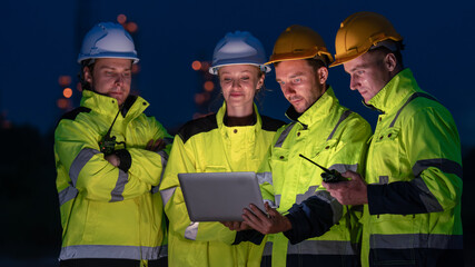 caucasian white engineers in safety uniforms and helmets using laptop and radio for site communication. Concept of teamwork, inspection, and operations at an industrial facility.Construction of Oil, 