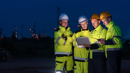 caucasian white engineers in safety uniforms and helmets using laptop and radio for site communication. Concept of teamwork, inspection, and operations at an industrial facility.Construction of Oil, 