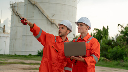 caucasian white engineers in safety uniforms and helmets using laptop and radio for site communication. Concept of teamwork, inspection, and operations at an industrial facility.Construction of Oil, 