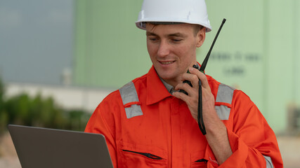 caucasian white engineers in safety uniforms and helmets using laptop and radio for site communication. Concept of teamwork, inspection, and operations at an industrial facility.Construction of Oil, 