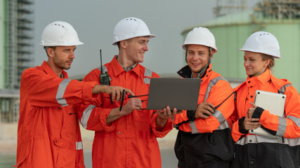 caucasian white engineers in safety uniforms and helmets using laptop and radio for site communication. Concept of teamwork, inspection, and operations at an industrial facility.Construction of Oil, 