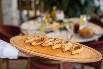 Close up view of a waiter holding baked, small portion Turkish pizza assortments with ground meat, cheese, and mixed on a wooden board in a restaurant.