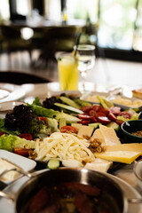 Close up view of a mix breakfast table with various foods, including cheese, lettuce, walnuts, tomatoes, cucumber, vegetables, and olives, in a restaurant.