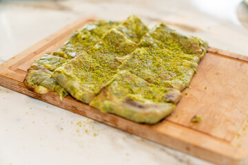 Traditional Turkish dessert Katmer with clotted cream and dough served on wooden board on a restaurant table. Prepared with thin dough, green ground pistachio and sherbet. Dessert of Gaziantep region.