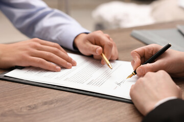 Man pointing at document and woman putting signature at wooden table, closeup