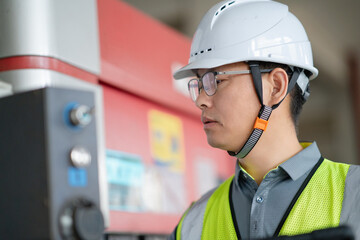 An Asian male engineer is holding a tablet in front of a bending machine.