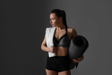 Sporty woman with terry towel and fitness mat on dark grey background