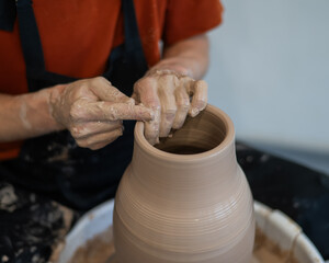 Close-up of a potter's hands making a ceramic vase on a potter's wheel. 