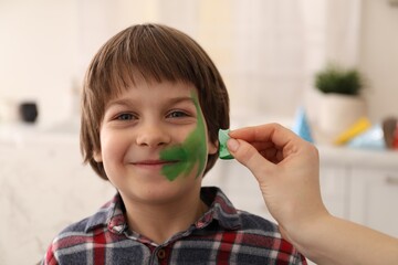 Animator drawing dinosaur on boy's face indoors, closeup