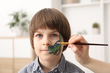 Animator drawing dinosaur on boy's face indoors, closeup