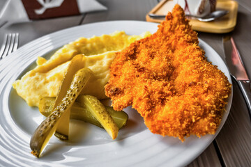 Fried pork schnitzel with mashed potato and pickled cucumber.