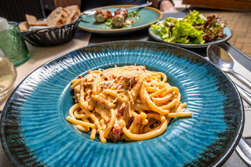 Spaghetti carbonara in blue plate, salad, bread, drink and pork roll, restaurant table.