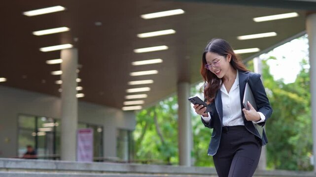 A pretty businesswoman wearing glasses uses her mobile phone, texts and cheats on her smartphone while walking in her office.
