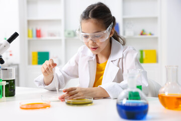 Little girl doing chemical experiment at desk indoors