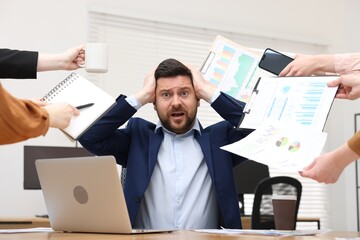 Man overwhelmed by different requests from colleagues at desk in office