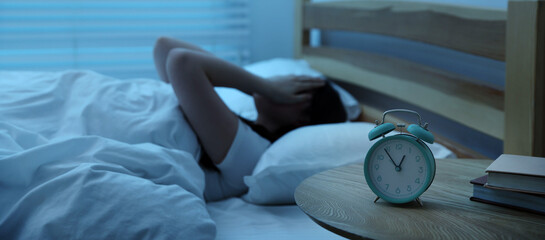Frustrated young woman suffering from insomnia on bed indoors, focus on alarm clock