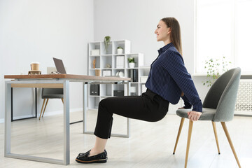 Beautiful woman exercising with chair in office