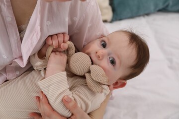 Mother and her cute little baby with rattle toy on bed at home, closeup