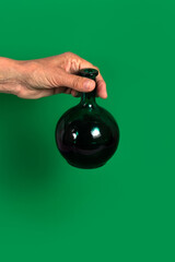 A woman's hand holding a round green glass bottle on a green background