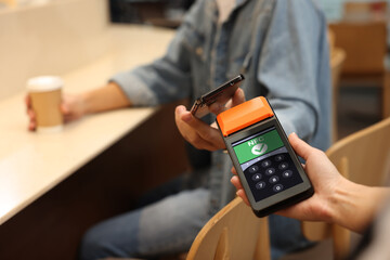 Payment terminal with NFC system. Client using credit card to pay for service in cafe, closeup