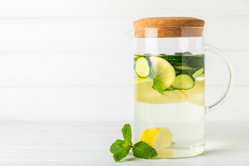Cucumber water with lemon, lime and mint on a wooden table. Water infused with sliced ​​cucumber in a drinking glass. Tonic refreshing drink. Cucumber lemonade.Summer natural cooling drink.Copy space