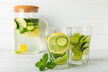 Cucumber water with lemon, lime and mint on a wooden table. Water infused with sliced ​​cucumber in a drinking glass. Tonic refreshing drink. Cucumber lemonade.Summer natural cooling drink.Copy space