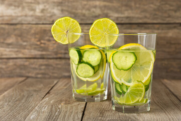 Cucumber water with lemon, lime and mint on a wooden table. Water infused with sliced ​​cucumber in a drinking glass. Tonic refreshing drink. Cucumber lemonade.Summer natural cooling drink.Copy space