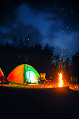 Camping tents and bonfire in wilderness at night under starry sky