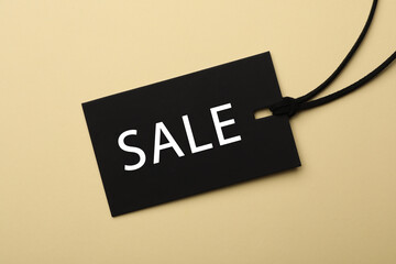 Black tag with word Sale on beige background, top view