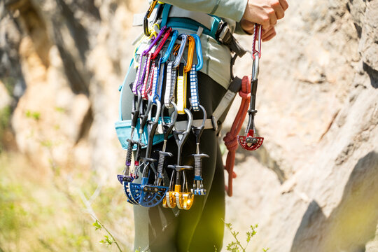 Female mountaineer with trad climbing rack. Climber in harness with spring-loaded cams, quick draws, slings and carabiners preparing for ascent in summer mountains. Friends, cam hex. Close-up