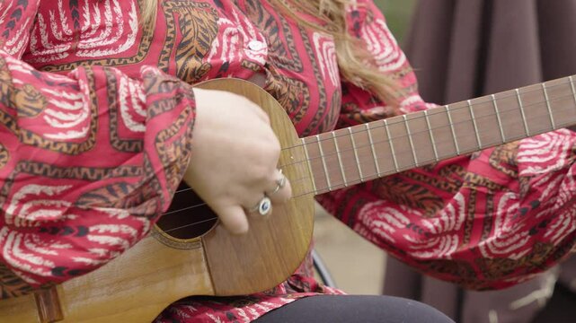 Close-up of a woman strumming a Traditional Colombo-Venezuelan Cuatro while wearing a red patterned blouse.