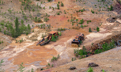 Rusty bulldozers represent the mining industry's past as pine trees thrive in the Falun copper mine in Sweden, showcasing nature's resilience and recovery over time