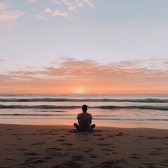 Fototapeta premium Man sitting on beach at sunset while meditating by the ocean 