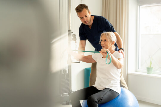 Senior woman working out with resistance band under the guidance of a physiotherapist during rehabilitation