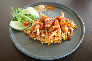 shrimp pad thai with savory sauce, garnished with fresh vegetables, sesame seeds, and herbs, beautifully plated on a dark ceramic dish.