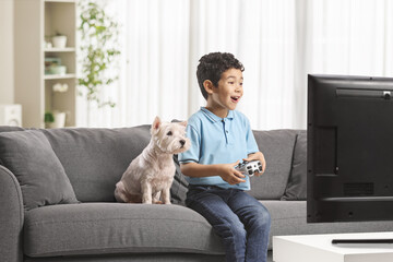 Happy asian kid with a dog sitting on a sofa and playing video games
