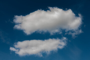 A pair of soft, white cumulus clouds float in a rich blue sky, creating a peaceful and minimal composition with ample copy space.