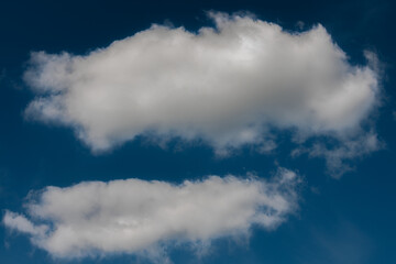 A pair of soft, white cumulus clouds float in a rich blue sky, creating a peaceful and minimal composition with ample copy space.