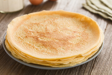 Stack of fresh homemade crepes, thin French-style pancakes, on plate with flour and eggs in the...